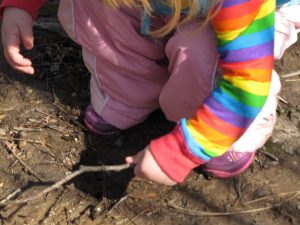 a squatting toddler pokes at mud with a stick