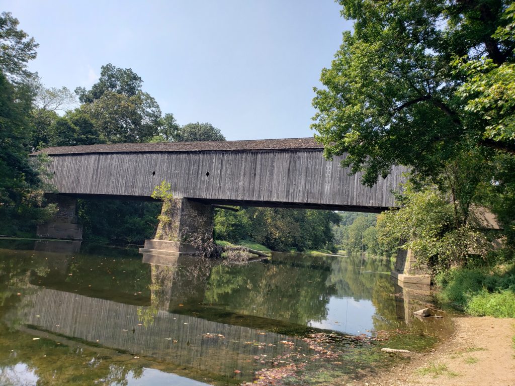 a gray covered bridge over a creek