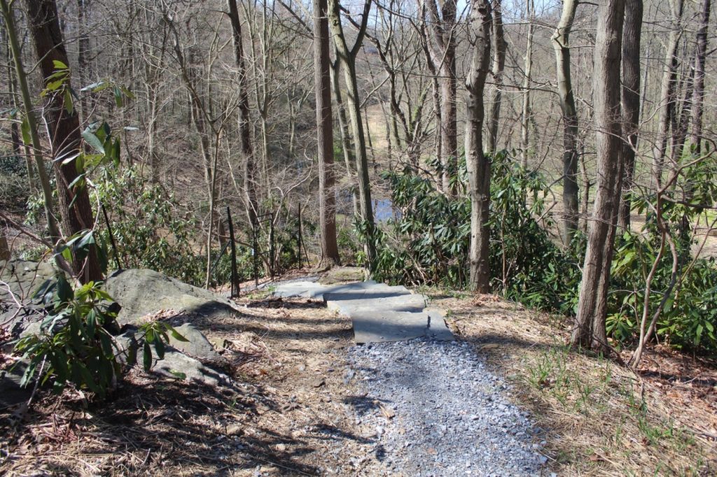 The trail in the foreground is crushed gray gravel, which changes to stone steps. Trees line both sides of the trail, a boulder sits to the left