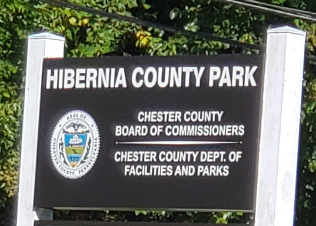 a brown sign across two white posts: "Hibernia County Park, Chester County Board of Commissioners, Chester County Dept. of Facilities and Parks"